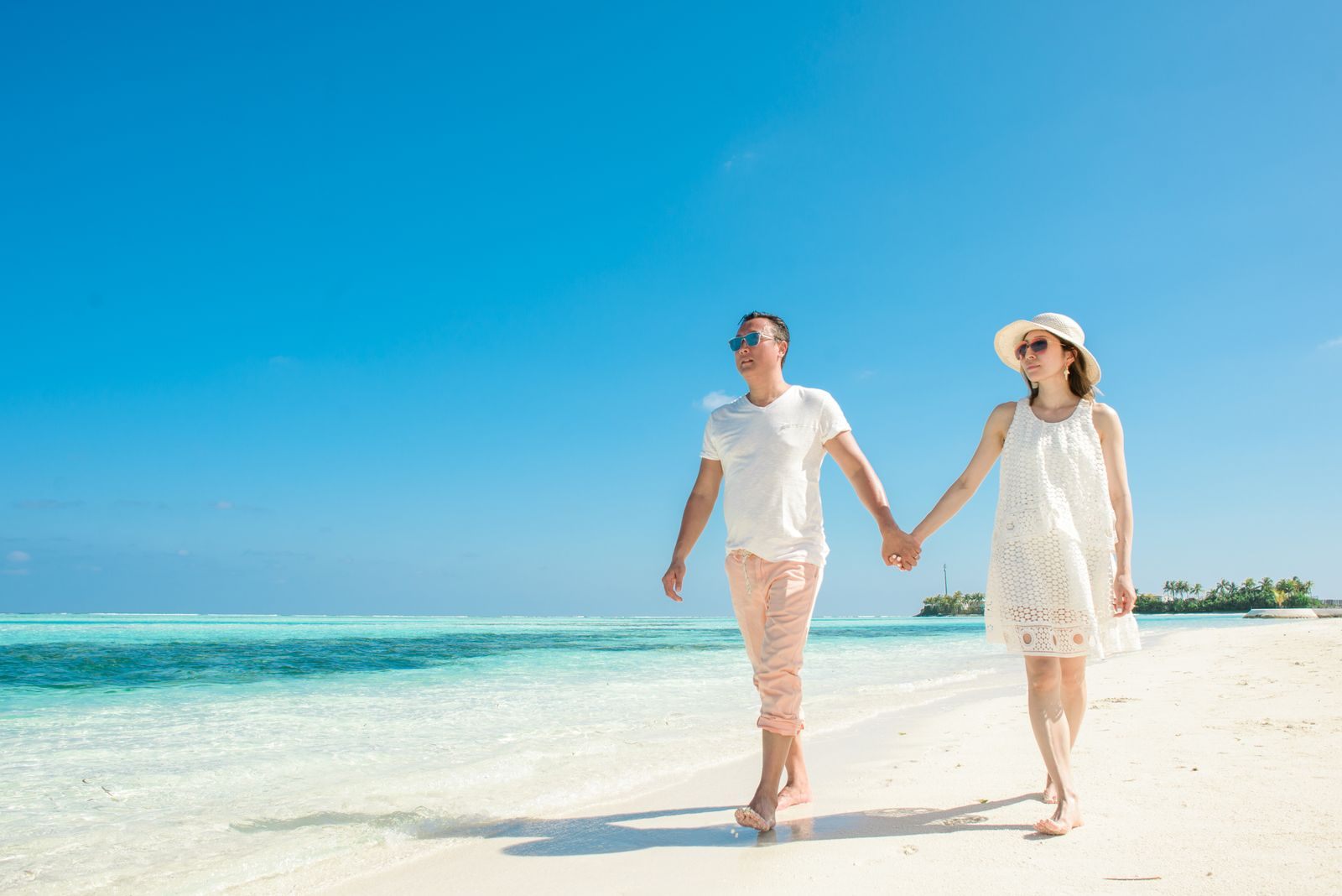 Couple in white holding hands on a tropical beach, the mood of the best honeymoon cruises